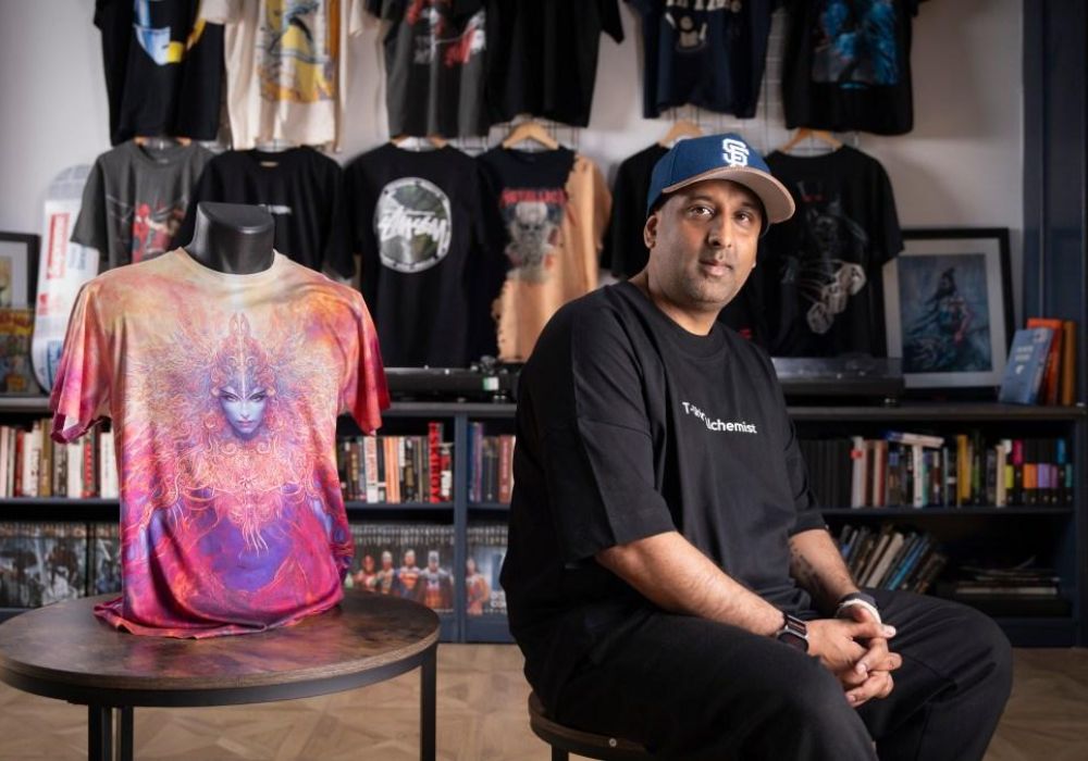 A Leicester garment manufacturer, Sunny P. of Meesha Group, sits beside a colourful T-shirt design in a studio setting. The photo highlights his recognition as part of Leicester’s Regional Rising Stars in UK textile manufacturing.